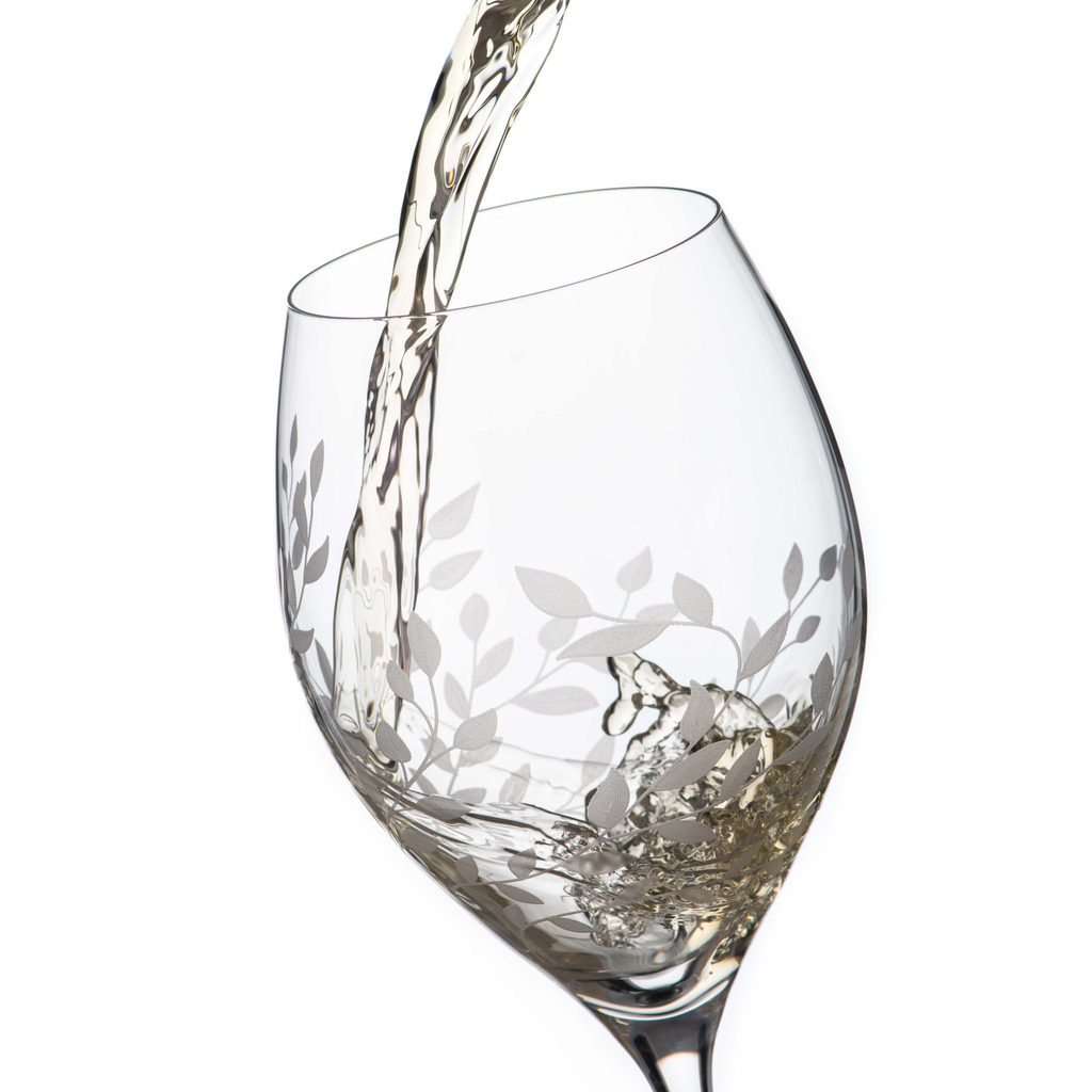 Wine glass with floral etching being filled with white wine on a white background