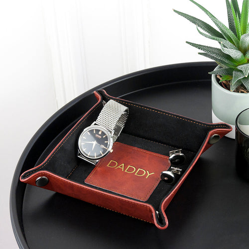 Tray with a watch and card on a black tray with a plant in the background