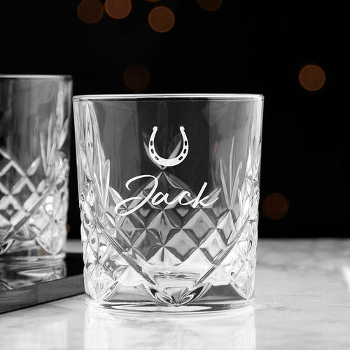 Crystal glass with engraved name and horseshoe symbol on a dark background