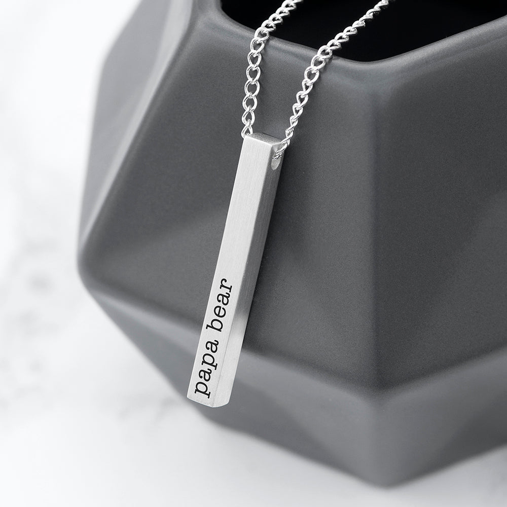 Silver necklace with 'papa bear' pendant on a gray geometric object