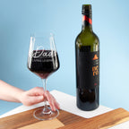Wine glass with 'Dad Living Legend' text and wine bottle on a wooden board against a blue background