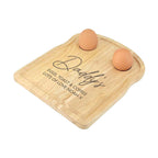 Wooden cutting board with 'Daddy's' engraving and two eggs on a white background