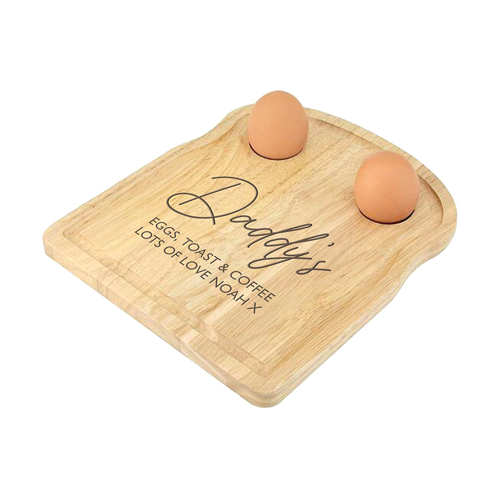 Wooden cutting board with 'Daddy's' engraving and two eggs on a white background
