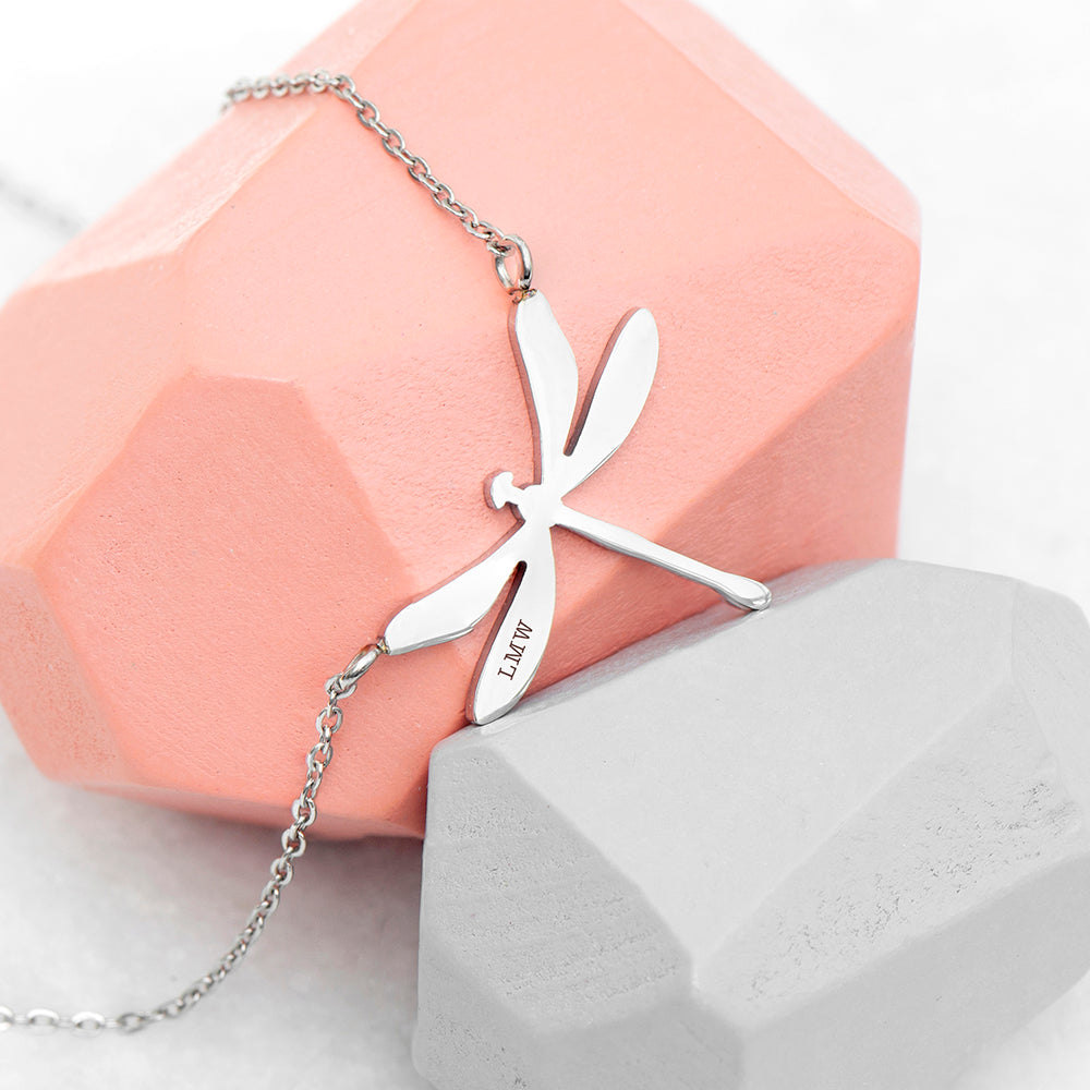 Silver dragonfly necklace on a pink and gray geometric background