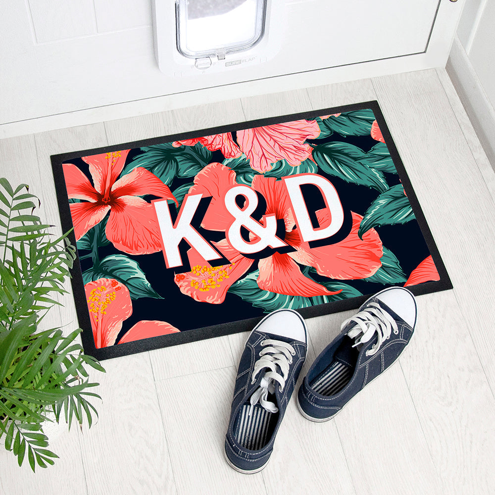 Floral doormat with initials 'K&D' on a white floor with shoes and plant.
