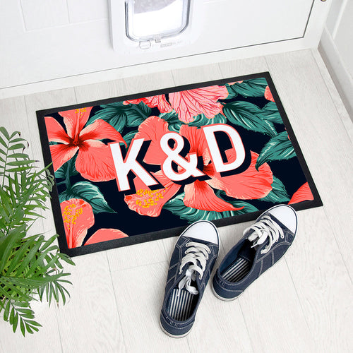 Floral doormat with initials 'K&D' on a white floor with shoes and plant.
