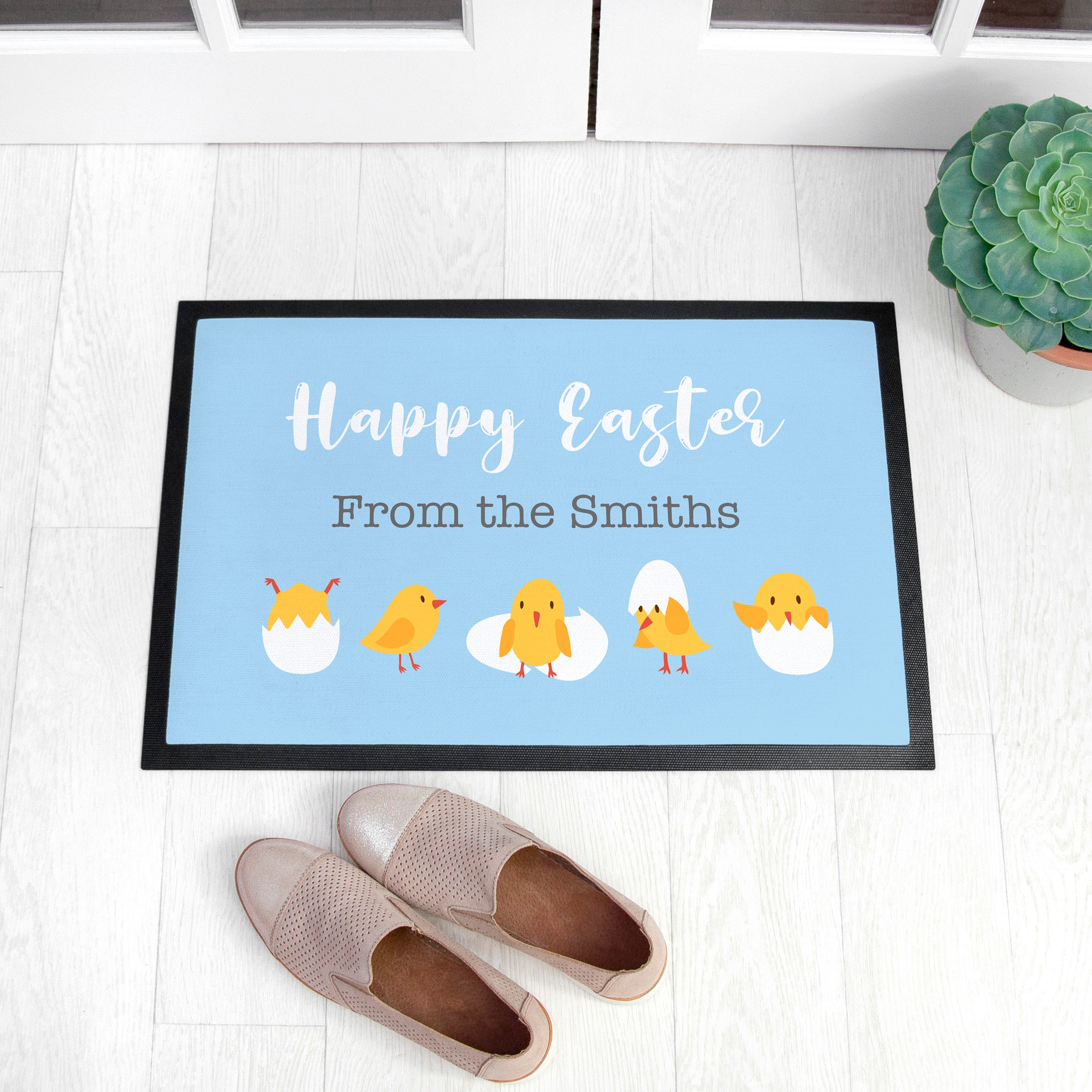 Doormat with 'Happy Easter From the Smiths' text and cartoon chicks on a light blue background, placed on a wooden floor.