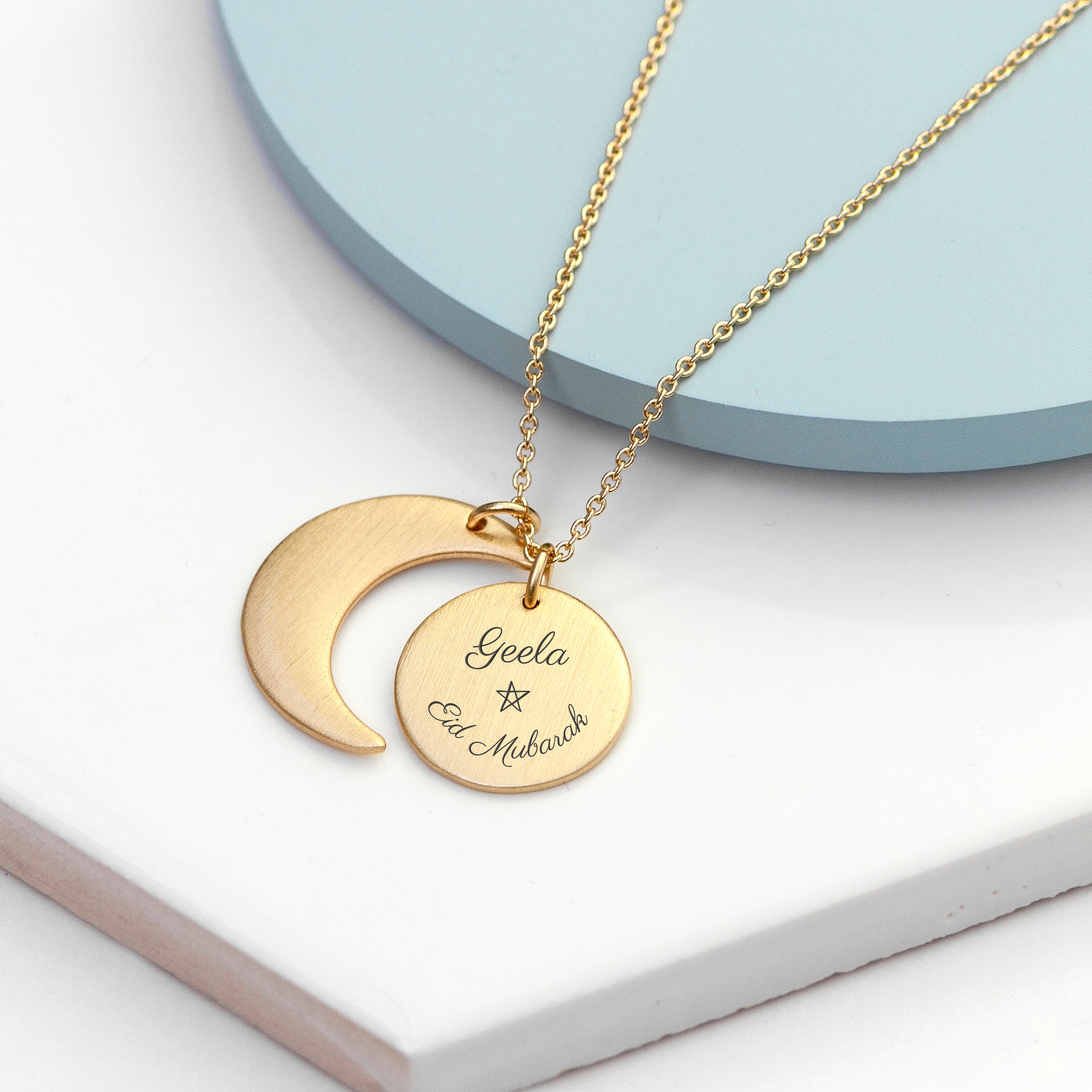 Gold necklace with a crescent moon and circular pendant on a light blue and white background