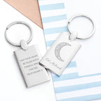 Two silver keychains with engraved text on a striped background