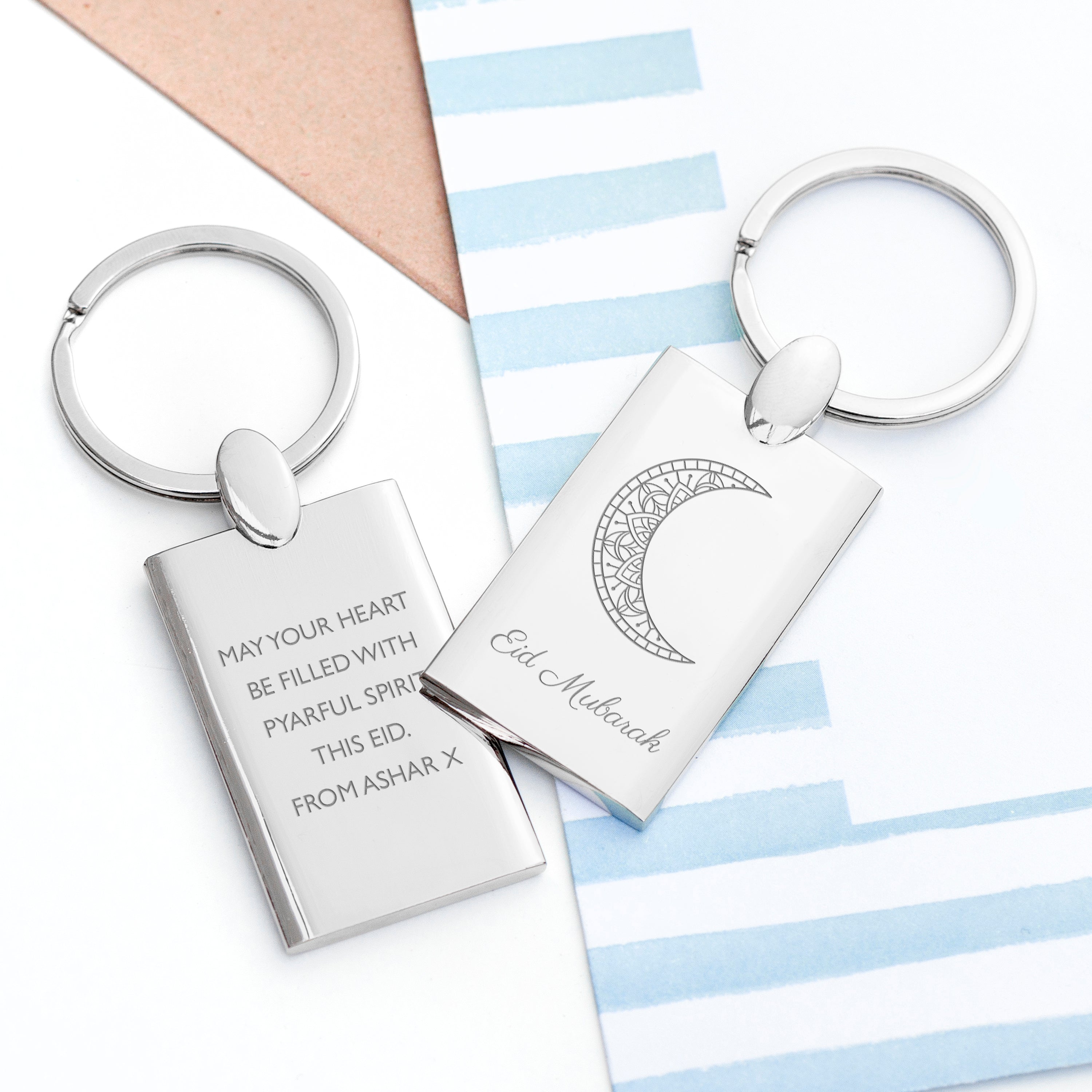 Two silver keychains with engraved text on a striped background