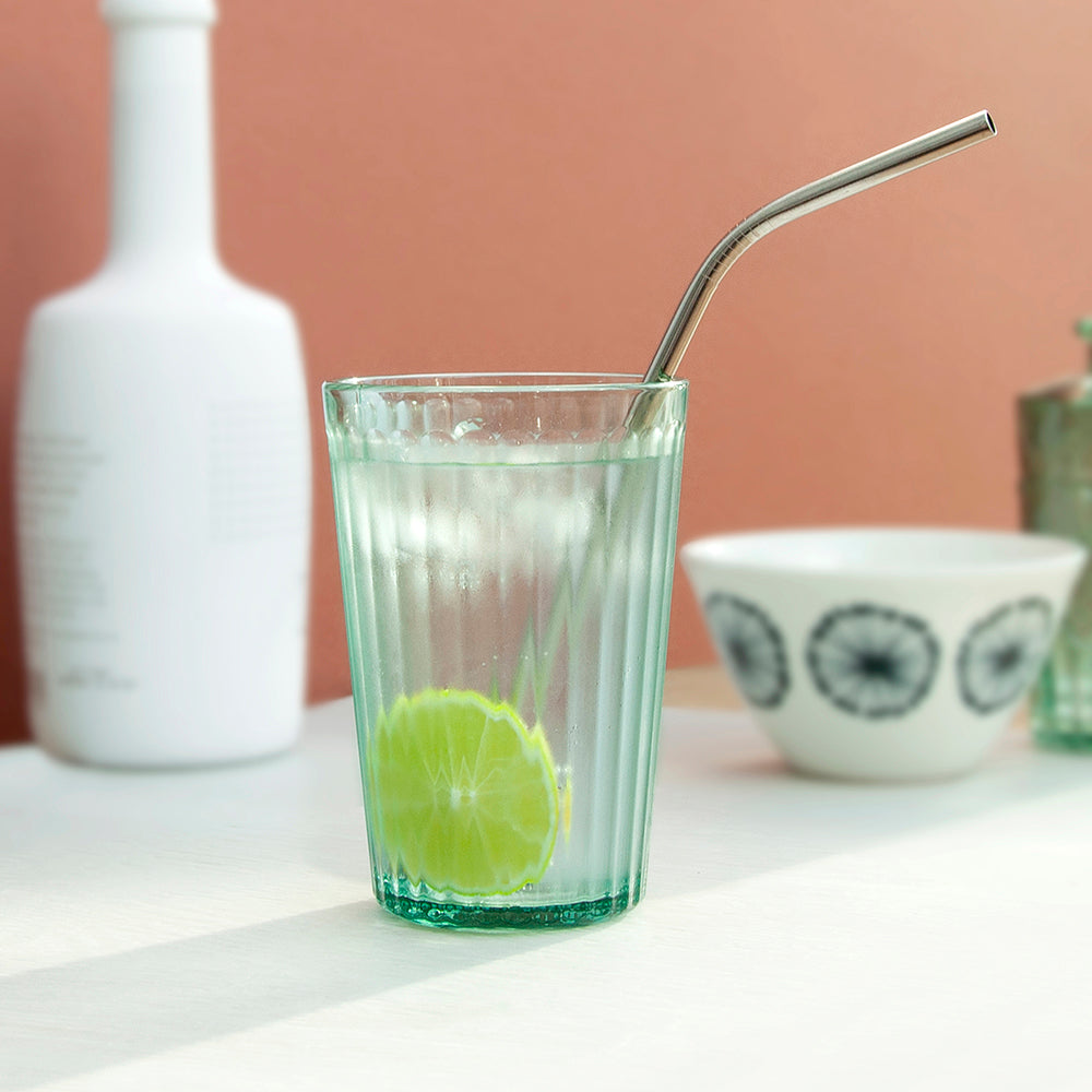 Clear glass with a lime wedge and metal straw on a white surface with a pinkish-beige background