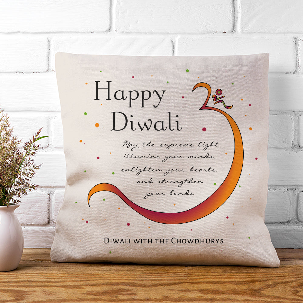 Decorative pillow with 'Happy Diwali' message on a wooden surface with a white brick wall background.