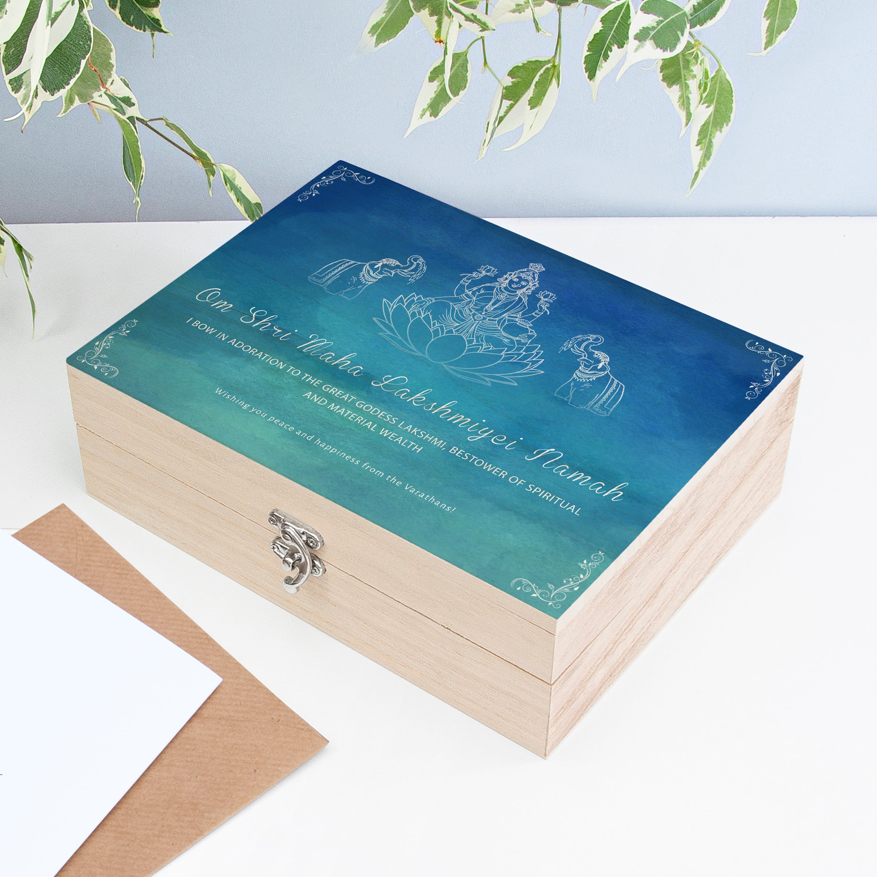 Wooden box with blue lid featuring engraved text and illustrations on a white surface with green leaves.
