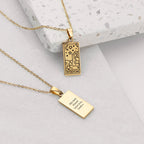 Gold necklace with two pendants on a light gray surface