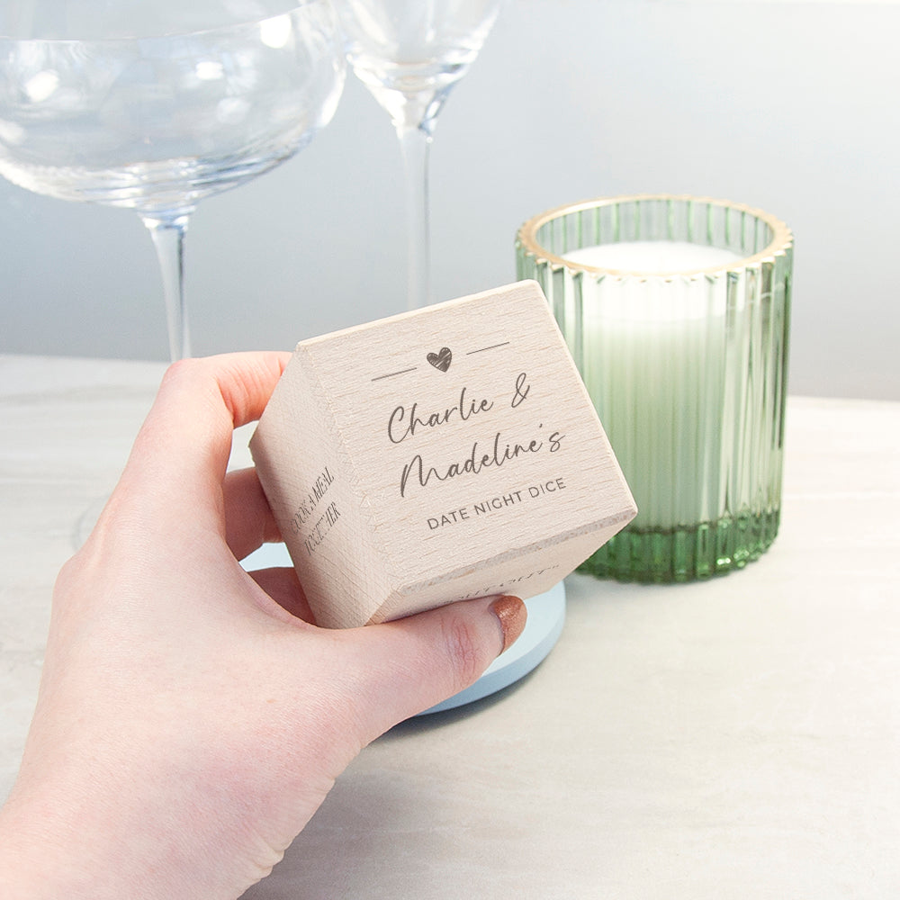 Hand holding a box labeled 'Charlie & Madeline's Date Night Dice' with a candle in the background.