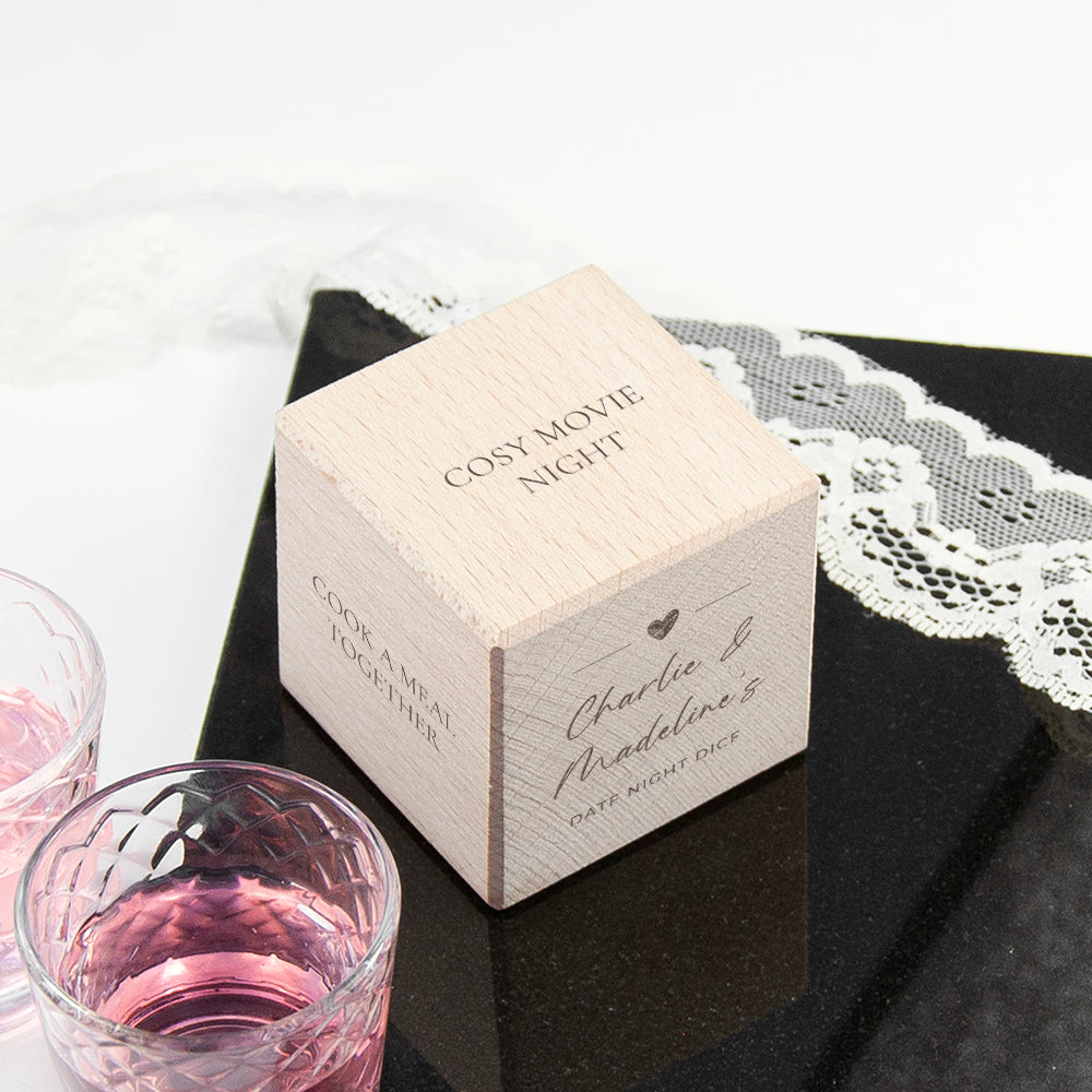 Wooden box labeled 'Cosy Movie Night' on a black surface with lace, next to pink drinks.