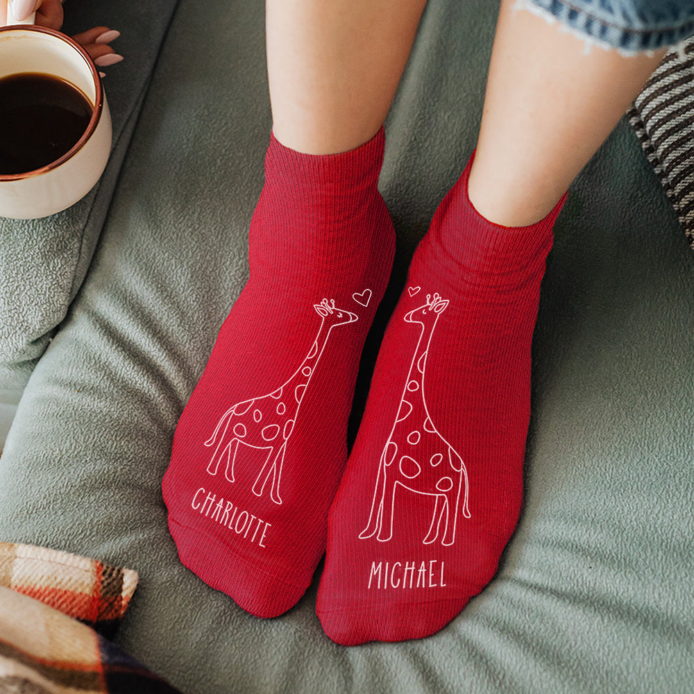 Red socks with giraffe designs and names 'Charlotte' and 'Michael' on a green surface.