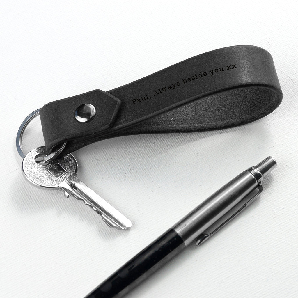 Black leather keychain with engraved text, keys, and a pen on a white background