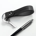 Black leather keychain with engraved text, keys, and a pen on a white background