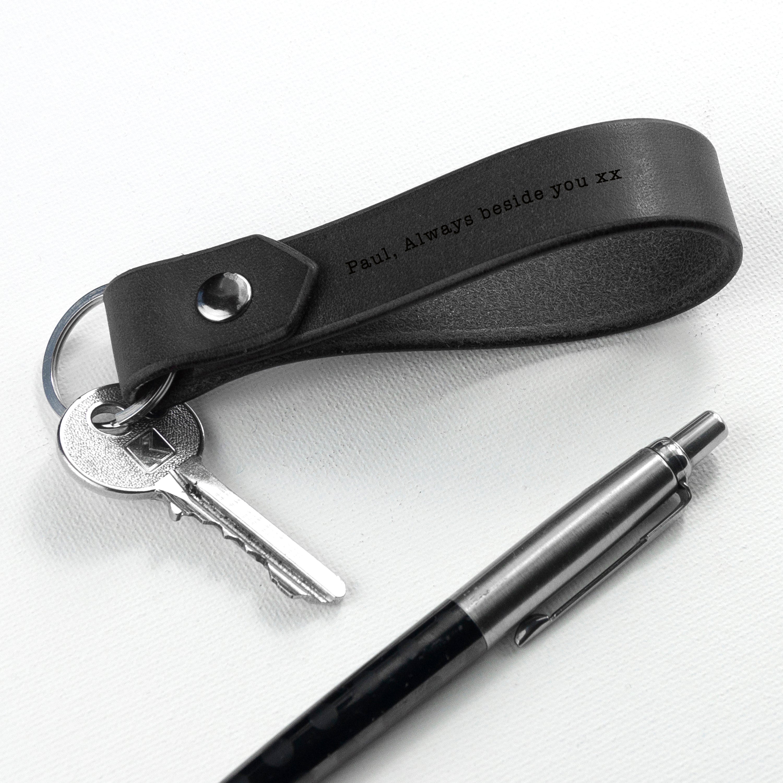 Black leather keychain with engraved text, keys, and a pen on a white background