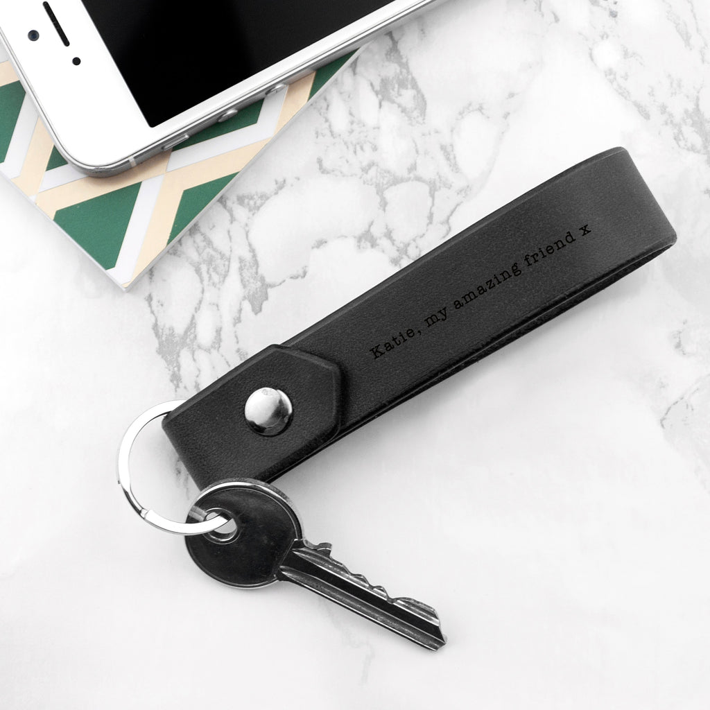 Black leather keychain with engraved text on a marble surface with a phone.