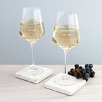 Two wine glasses with white wine on marble coasters, with 'LEAH & JOH' and 'EST. 2023' text.