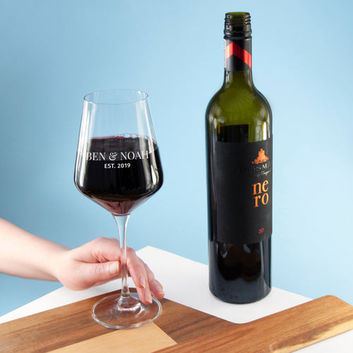 Bottle of Nero wine and a glass with 'Ben & Noah' branding on a wooden board against a blue background.