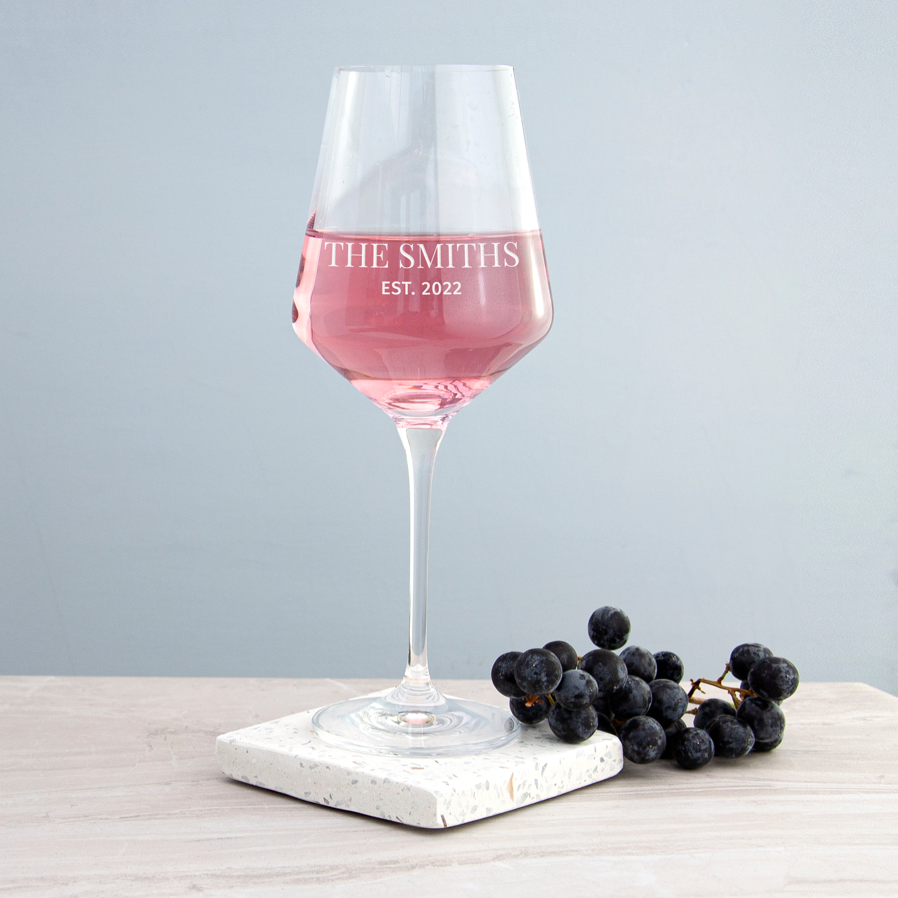 Wine glass with pink liquid and 'Mrs Stevenson' text on a marble coaster with grapes.