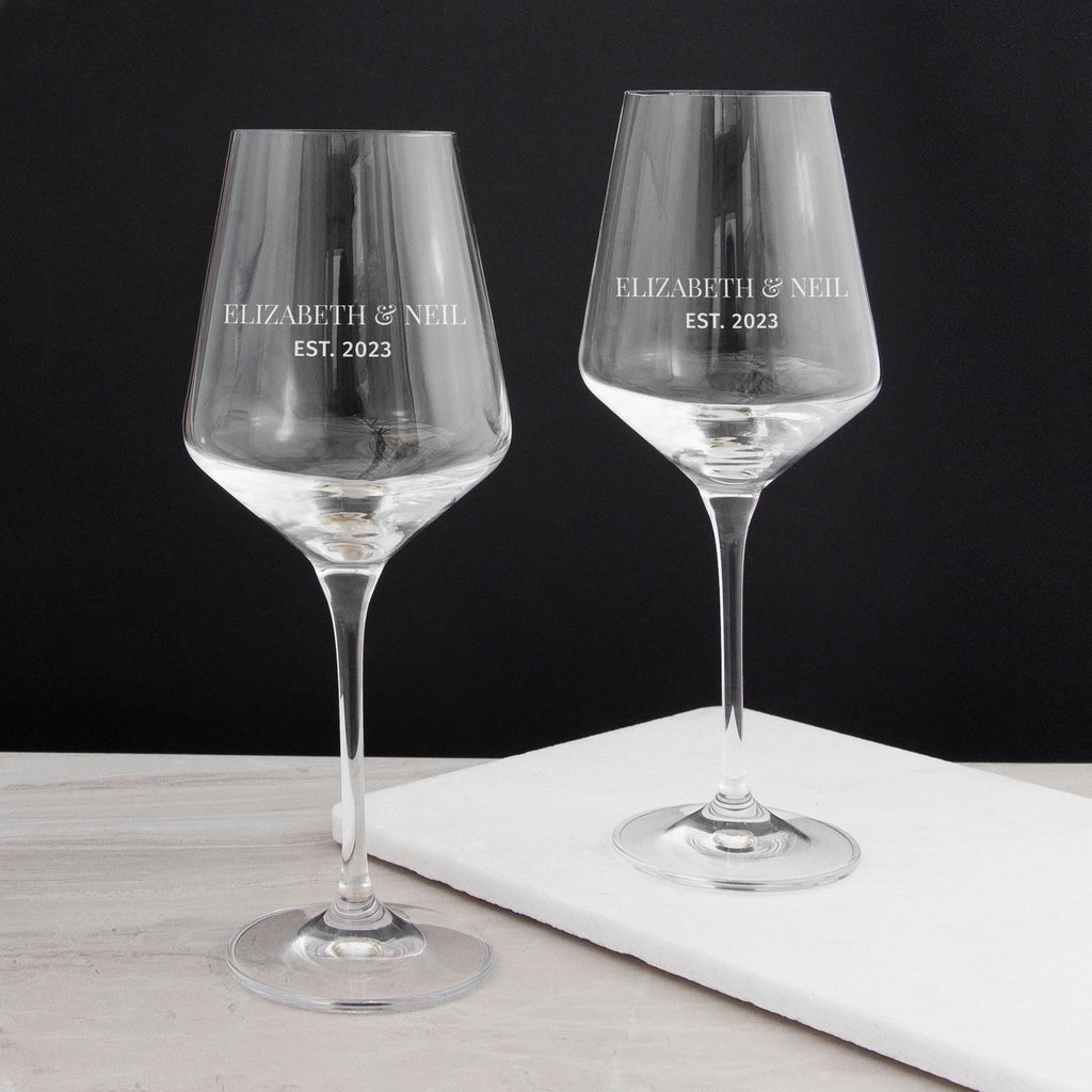 Two personalized wine glasses with 'Elizabeth & Neil EST. 2023' text on a black background.