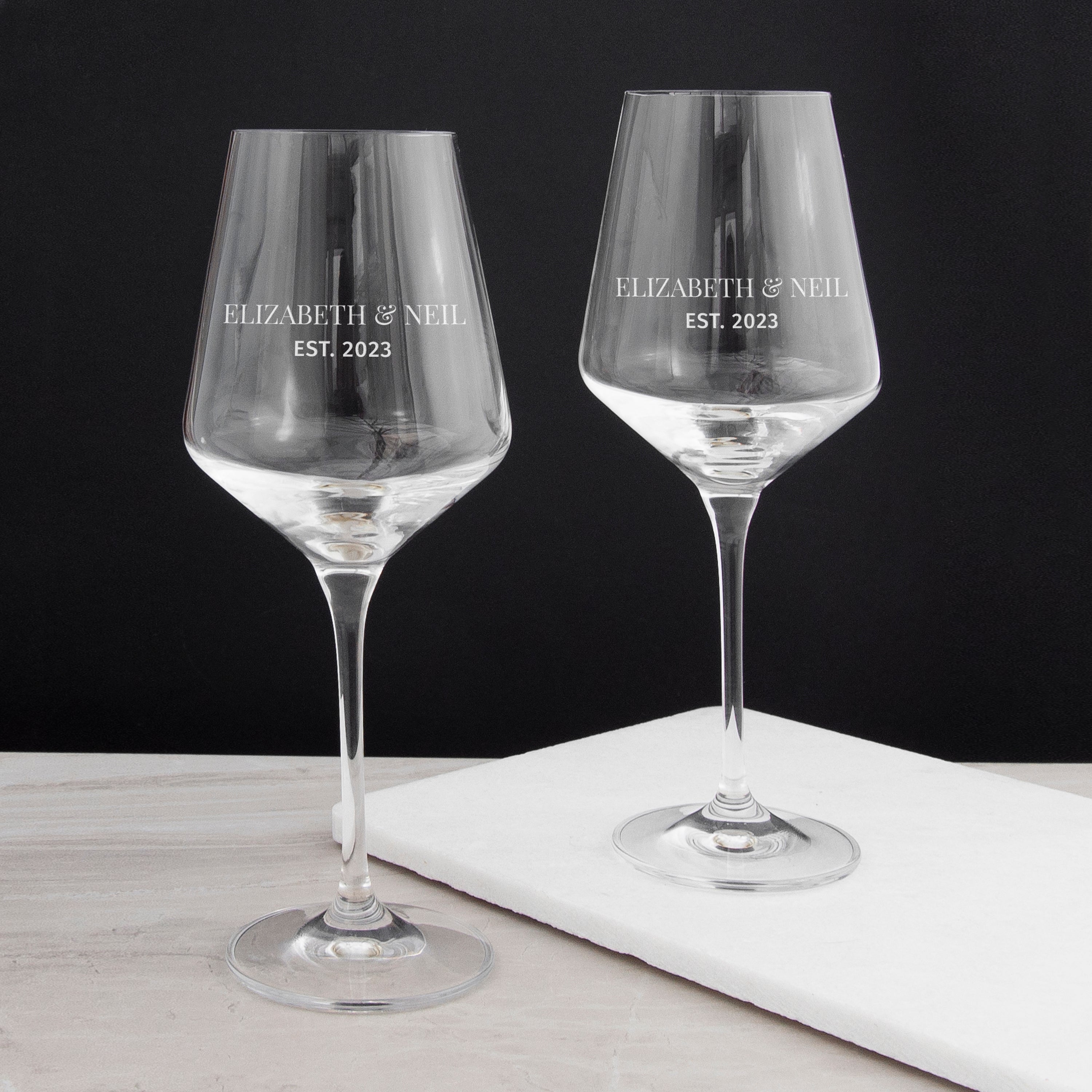 Two personalized wine glasses with 'Elizabeth & Neil EST. 2023' text on a black background.