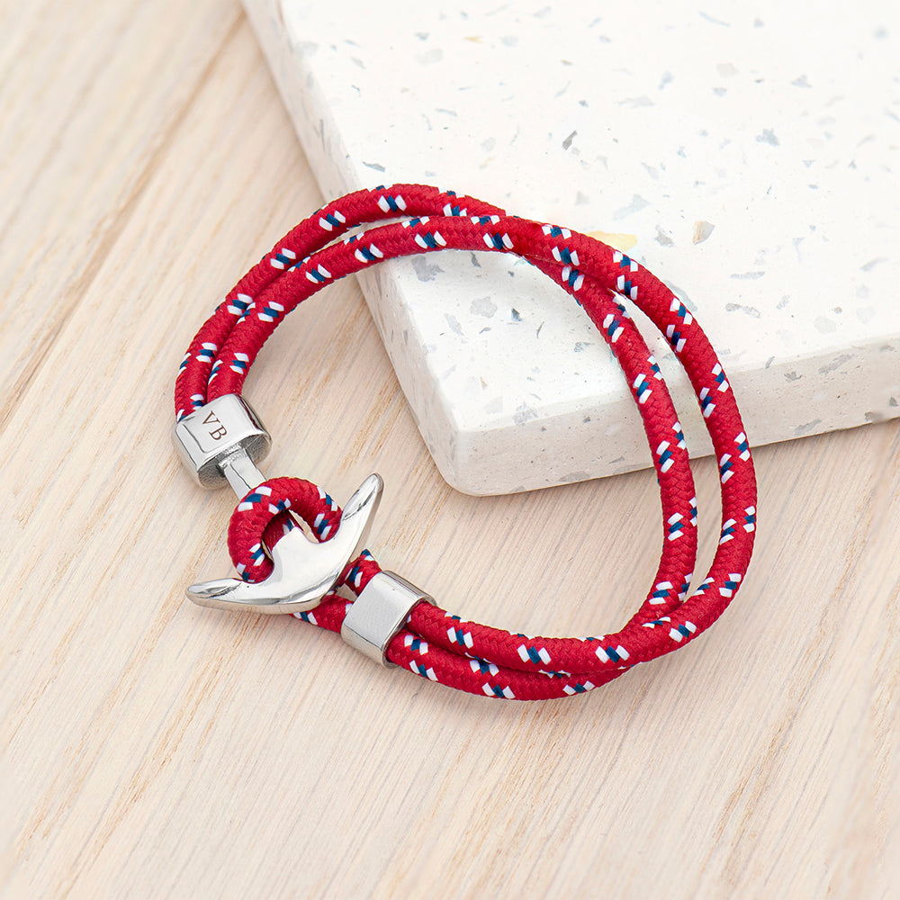 Red braided bracelet with silver anchor clasp on a light wooden surface