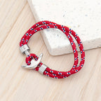 Red braided bracelet with silver anchor clasp on a light wooden surface