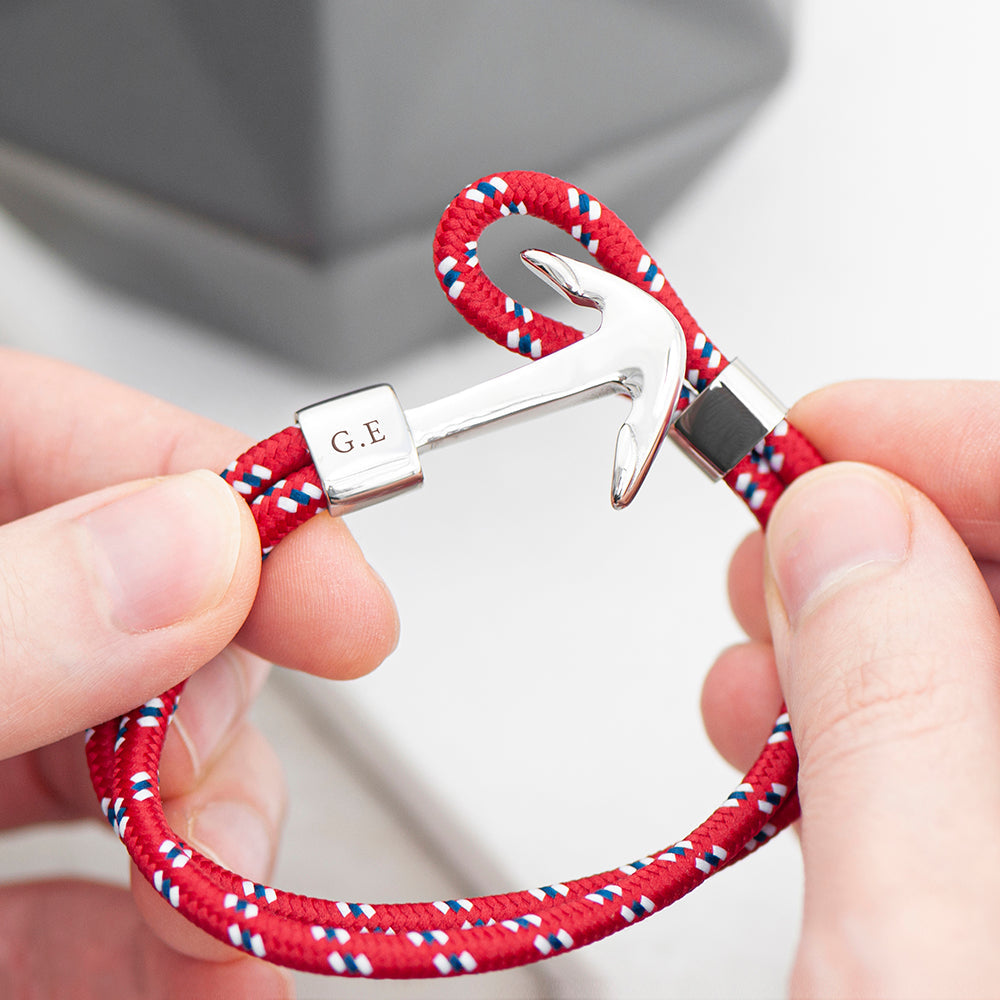 Red and white braided keychain with silver anchor clasp held by hands on a neutral background