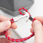 Red and white braided keychain with silver anchor clasp held by hands on a neutral background