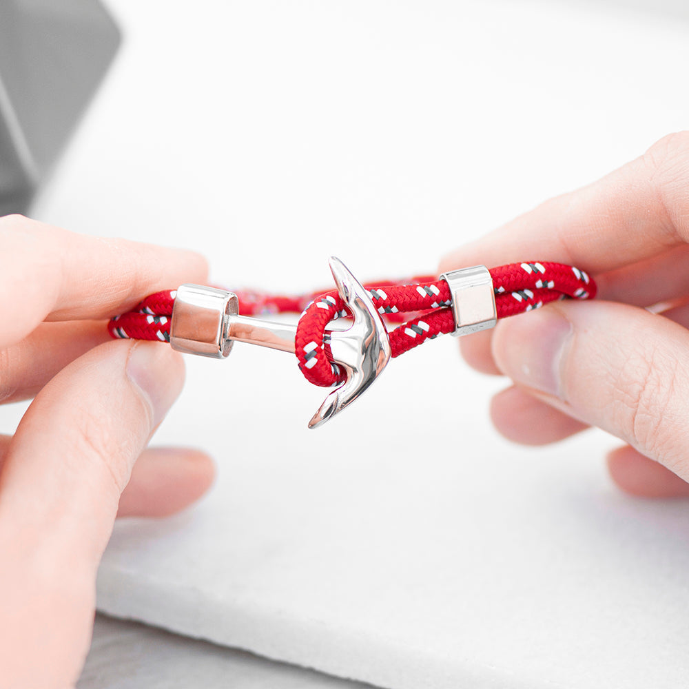 Red braided bracelet with silver anchor charm held by hands on a light background