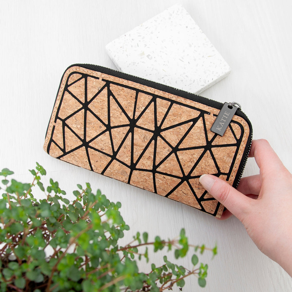 Cork wallet with geometric pattern held by a hand on a white surface with a plant in the foreground