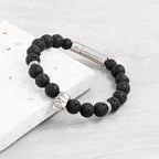 Black beaded bracelet with silver clasp on a light gray surface