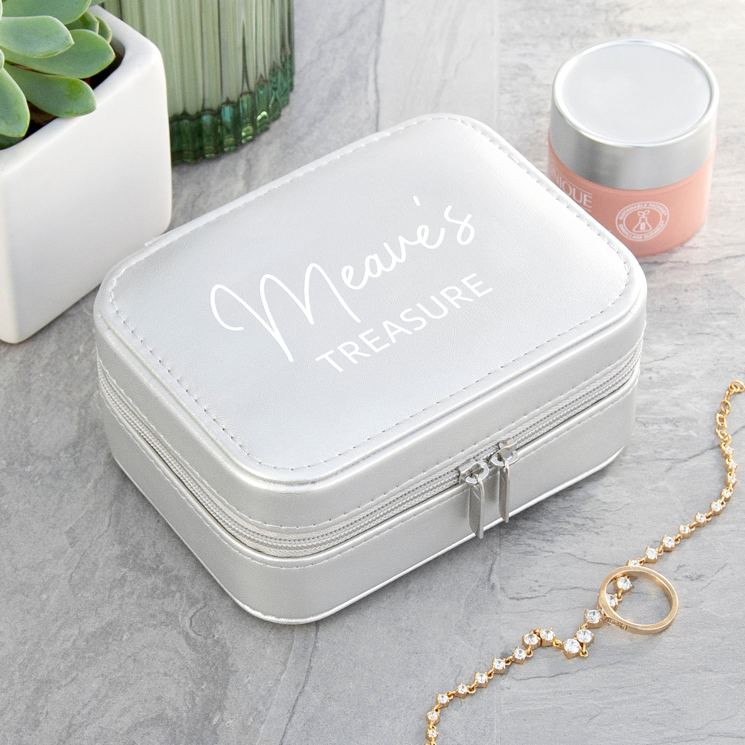 White jewelry box with 'Meave's Treasure' engraving on a gray surface with a gold necklace.