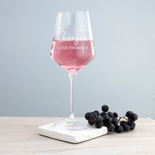 Wine glass with pink liquid on a marble coaster with grapes, against a light gray background