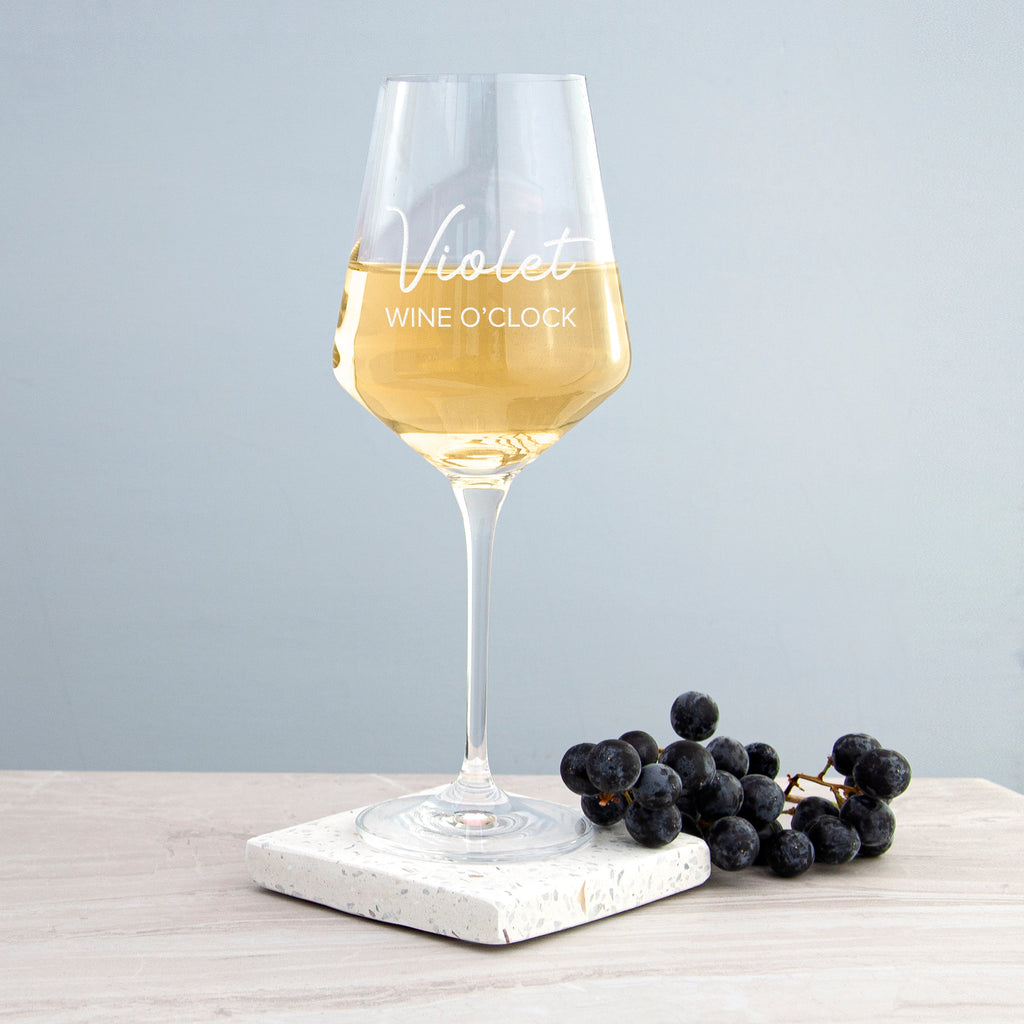 Wine glass with 'Violet Wine O'Clock' text on a marble coaster with grapes, against a light gray background.