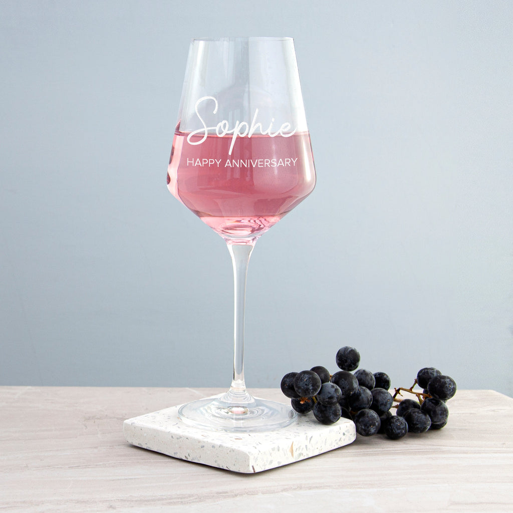Wine glass with pink liquid on a marble coaster with grapes, against a light gray background