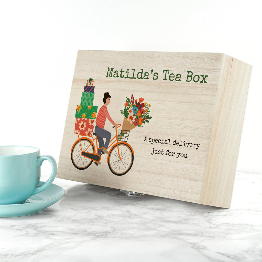 Wooden tea box with bicycle illustration and 'Matilda's Tea Box' branding on a marble surface with a teal cup.
