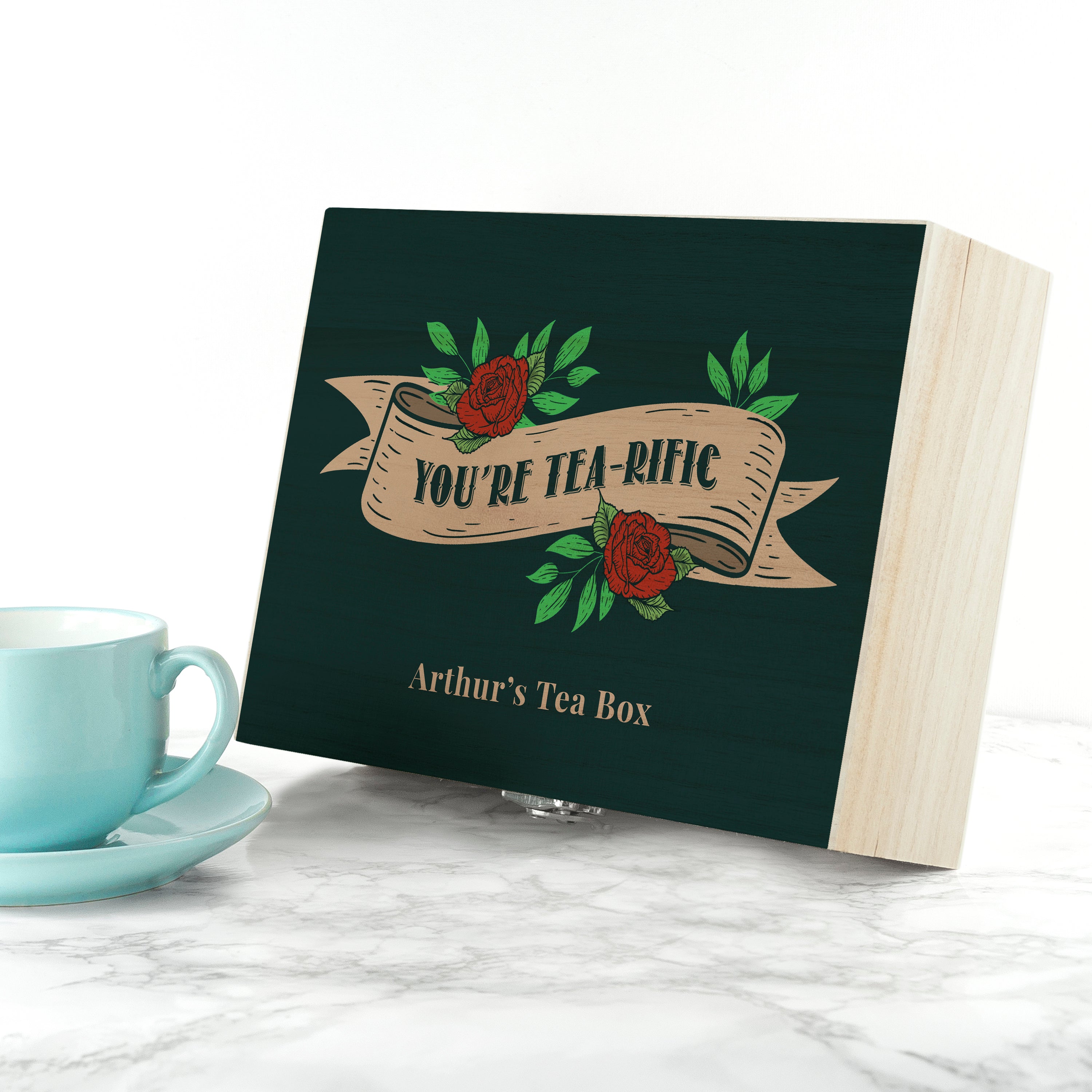 Tea box with 'You're Tea-rific' design next to a turquoise cup on a marble surface