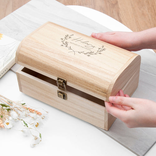 Wooden box with 'Olivia's Travel Memories' engraving on a light surface with hands opening it.
