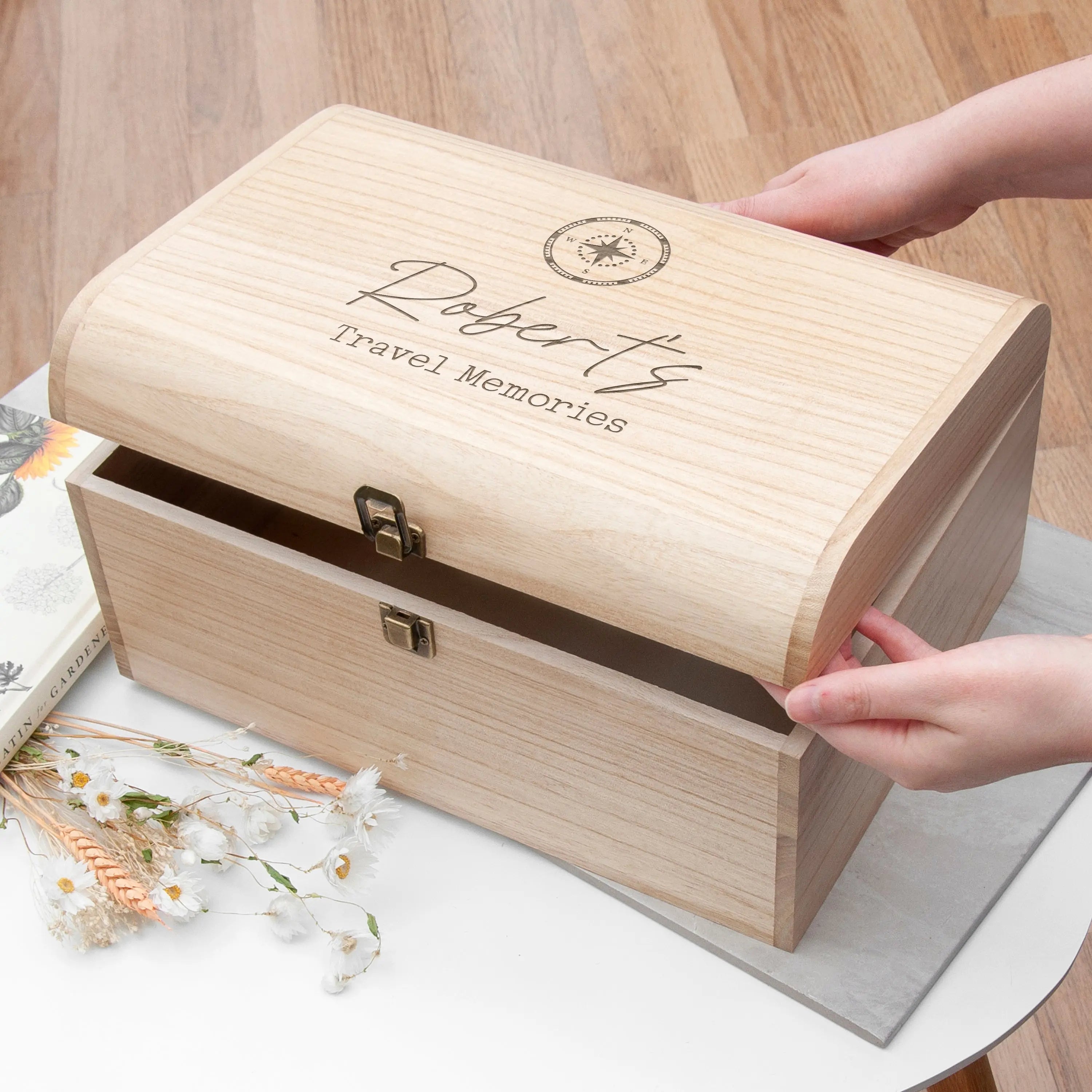Wooden box labeled 'Robert's Travel Memories' on a wooden surface with hands holding it open.