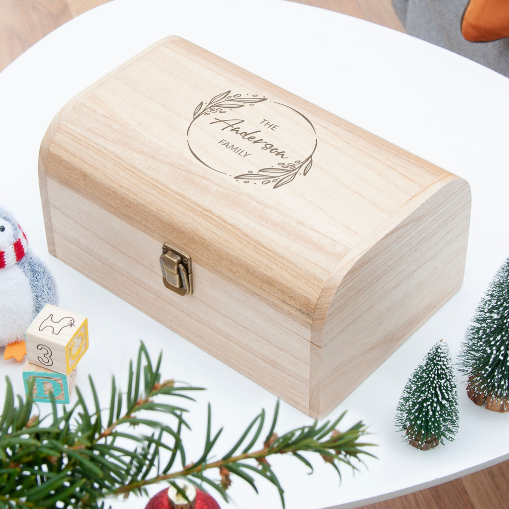 Wooden box with engraved text on a white surface with Christmas decorations.
