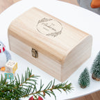 Wooden box with engraved text on a white surface with Christmas decorations.