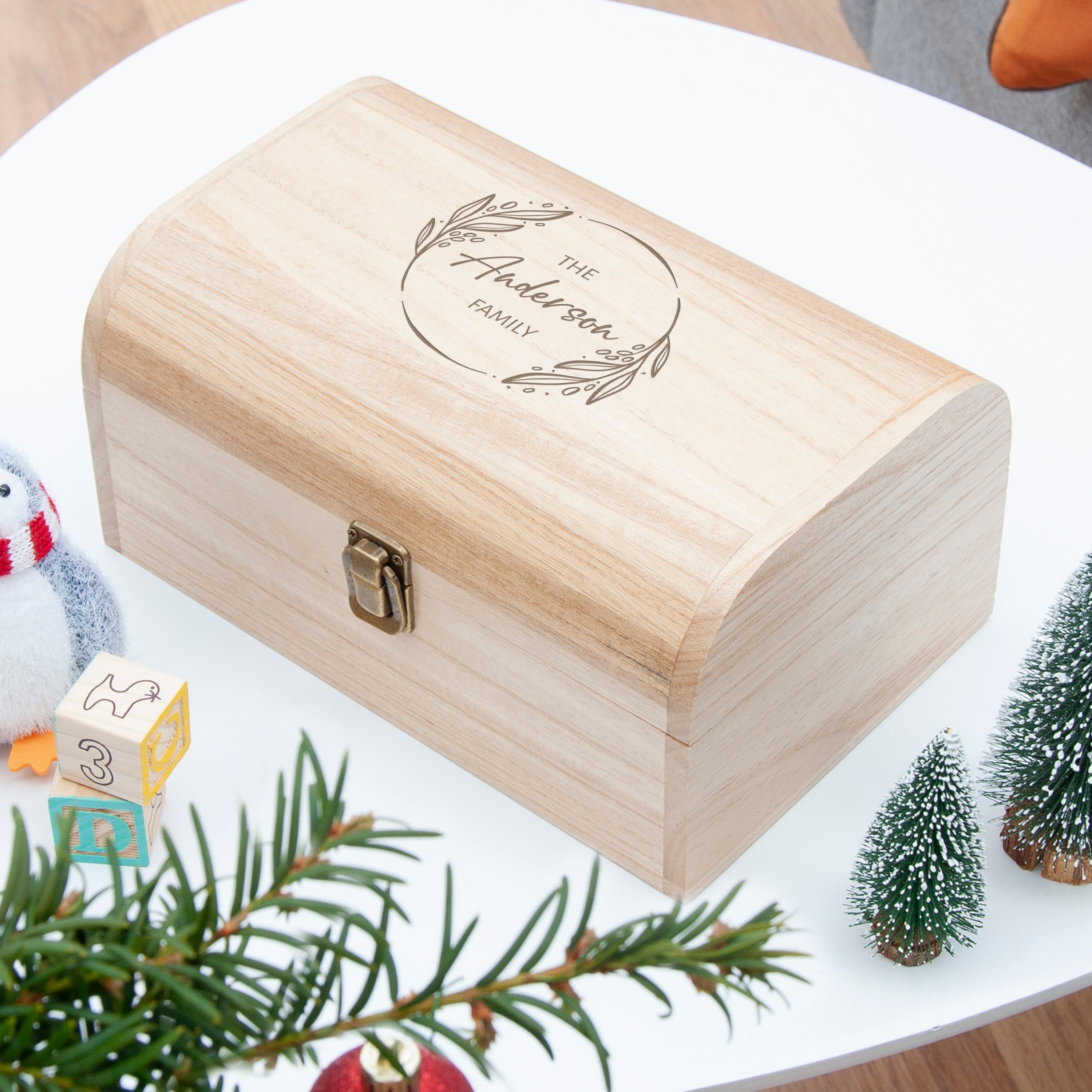 Wooden box with engraved text on a white surface with Christmas decorations.