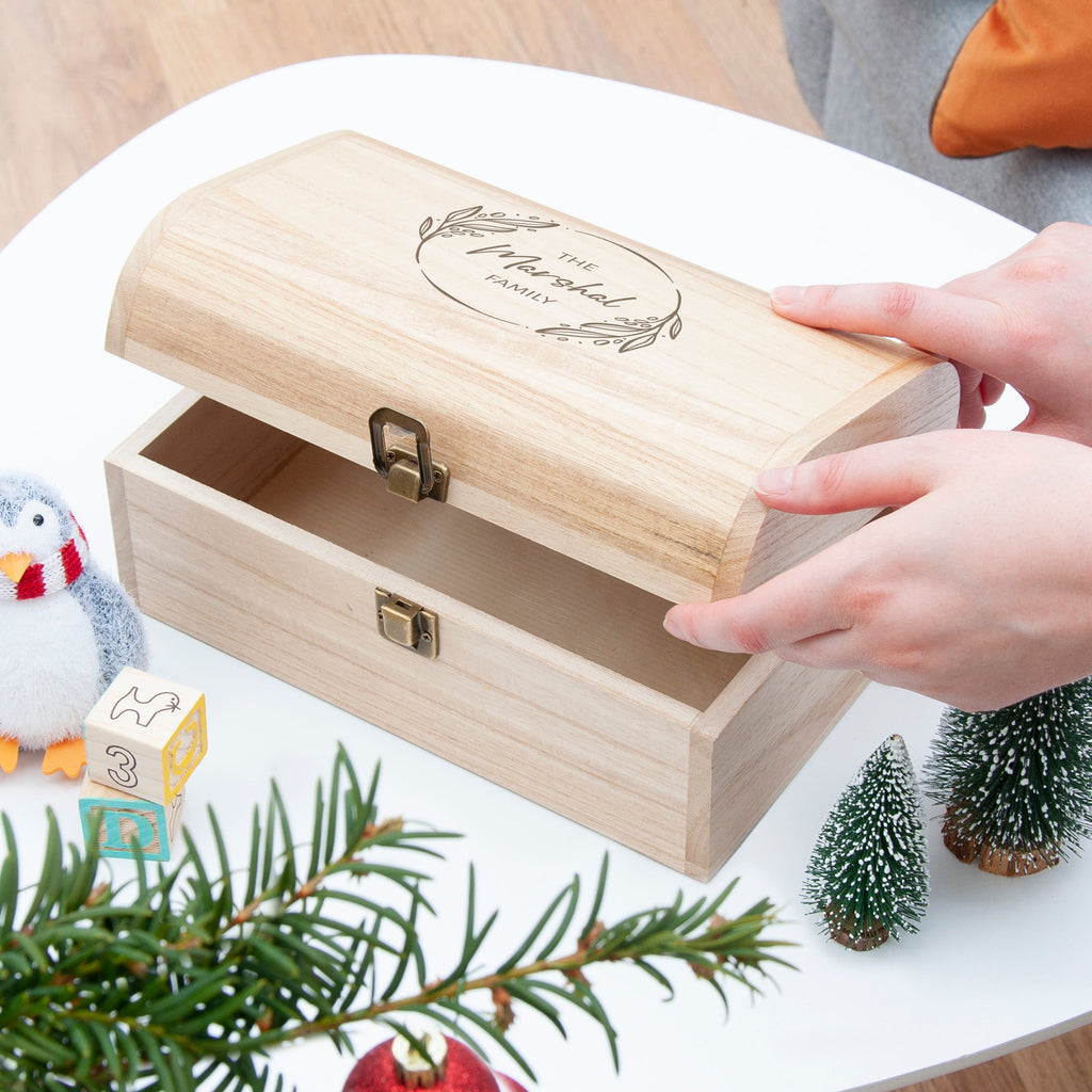 Wooden jewelry box with a hand opening it, surrounded by Christmas decorations.