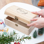 Wooden jewelry box with a hand opening it, surrounded by Christmas decorations.